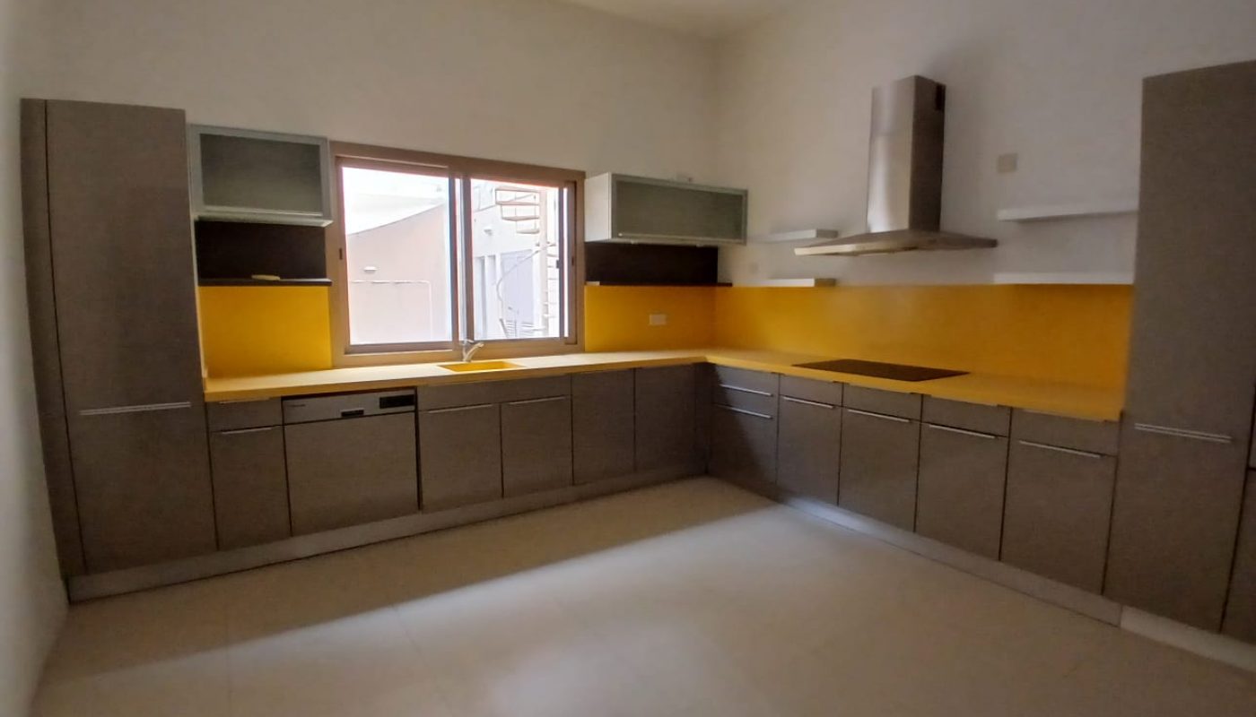 Modern kitchen with grey cabinets, yellow backsplash, a window over the sink, and built-in appliances arranged in an L-shaped layout.