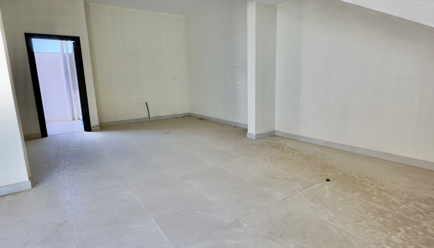 Empty room with tiled floors, cream-colored walls, an open doorway, and a staircase with black railing on the right side.