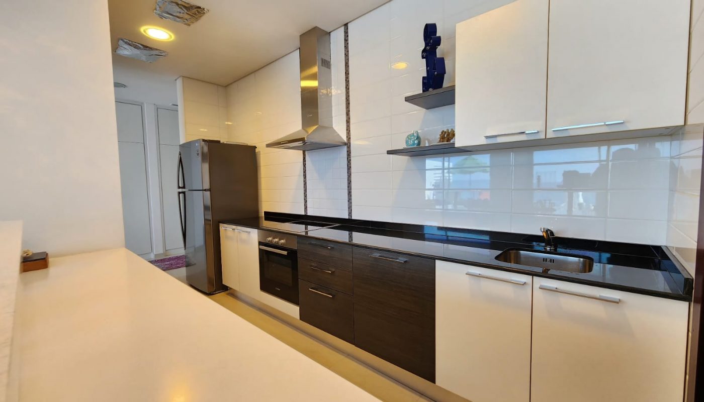 Modern kitchen with white and dark cabinets, stainless steel appliances, a built-in oven, electric cooktop, refrigerator, sink, and open shelves with decorative items.