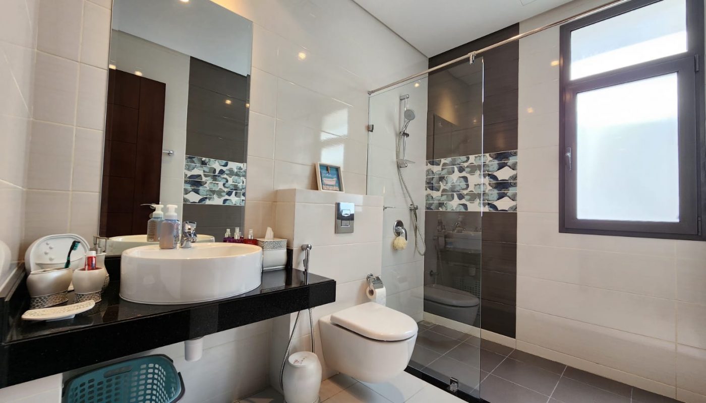 Modern bathroom with white tiles, a glass shower enclosure, wall-mounted toilet, countertop sink, mirror, and a window providing natural light.