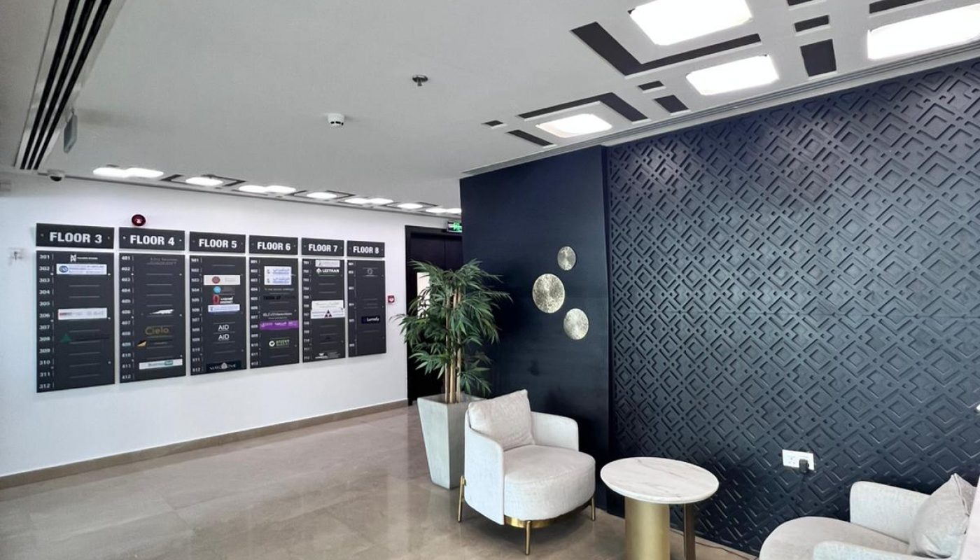 Modern office lobby with two armchairs, a small round table, a plant, and directory boards listing floor information on the back wall.
