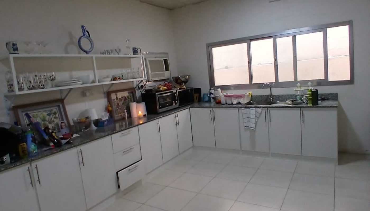 Spacious kitchen with white cabinets, tiled floor, shelves with kitchenware, large window, ceiling fan, and various appliances on the countertop.