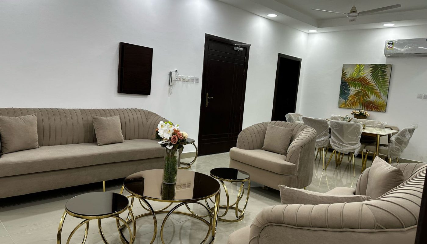 Modern living and dining room with beige furniture, round glass coffee tables, a flower vase, wall art, and ceiling lights.