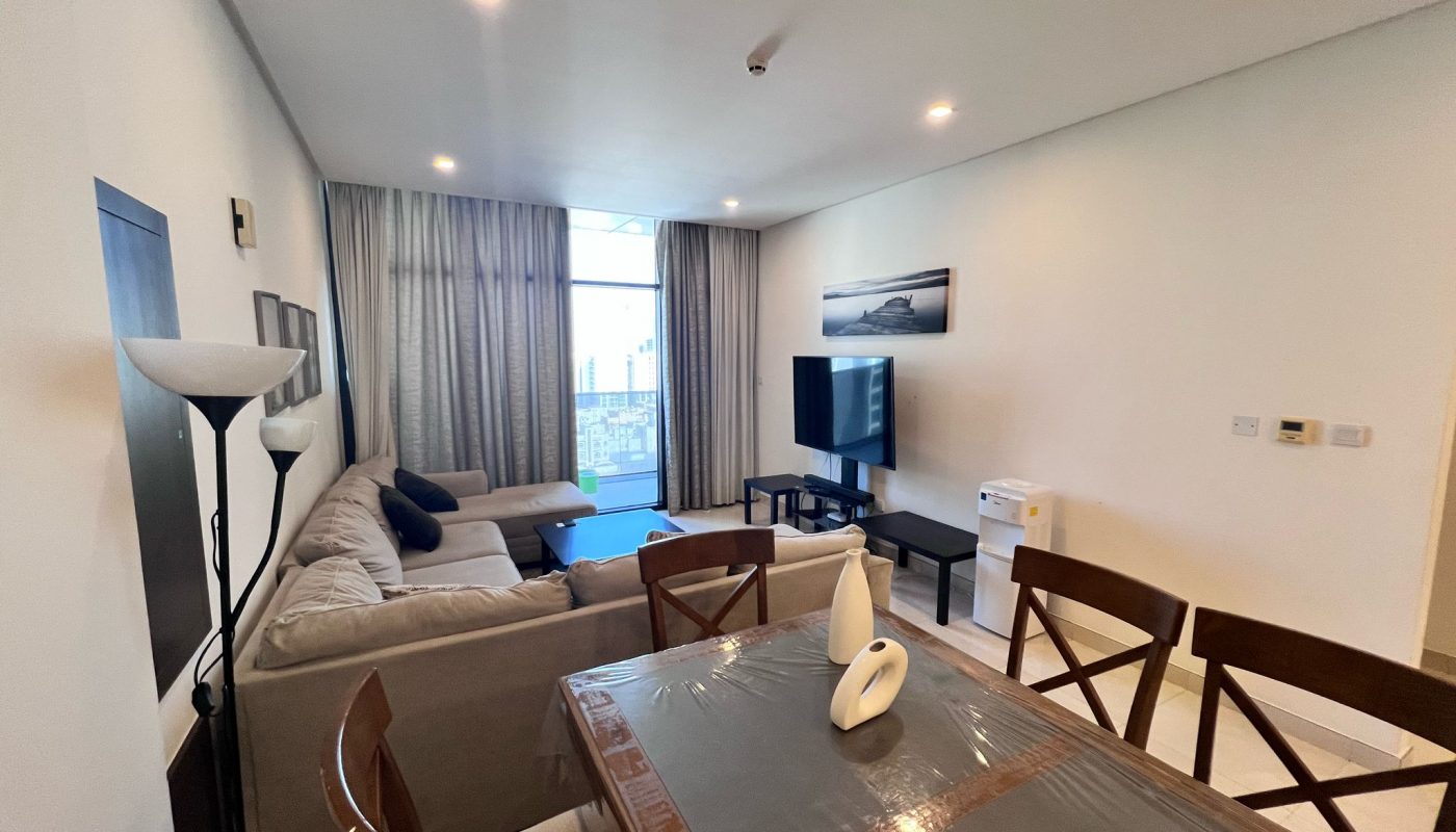 A modern living and dining area with a sectional sofa, TV, dining table with four chairs, floor lamp, and large window with city view.