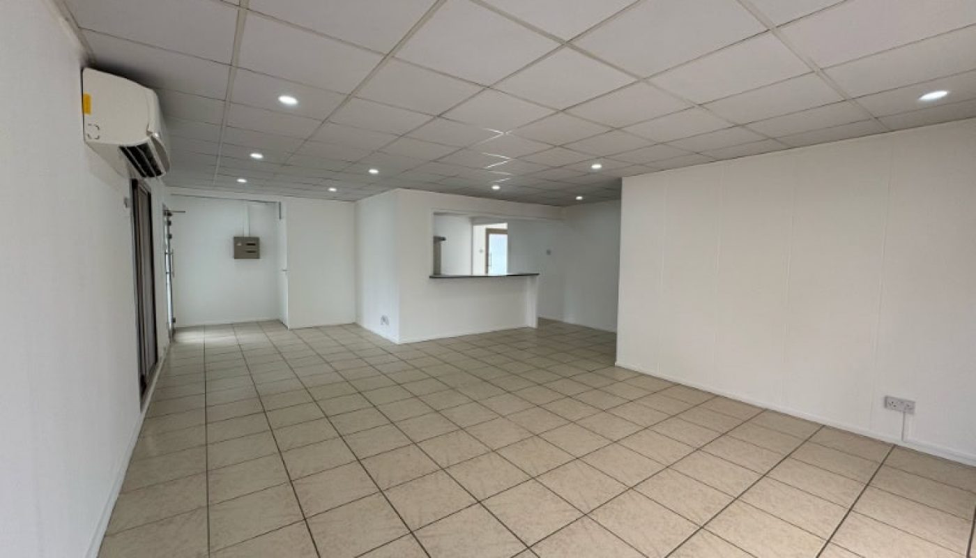 Empty room with tiled floor, white walls, recessed ceiling lights, air conditioning unit, and a small counter opening to an adjoining space.