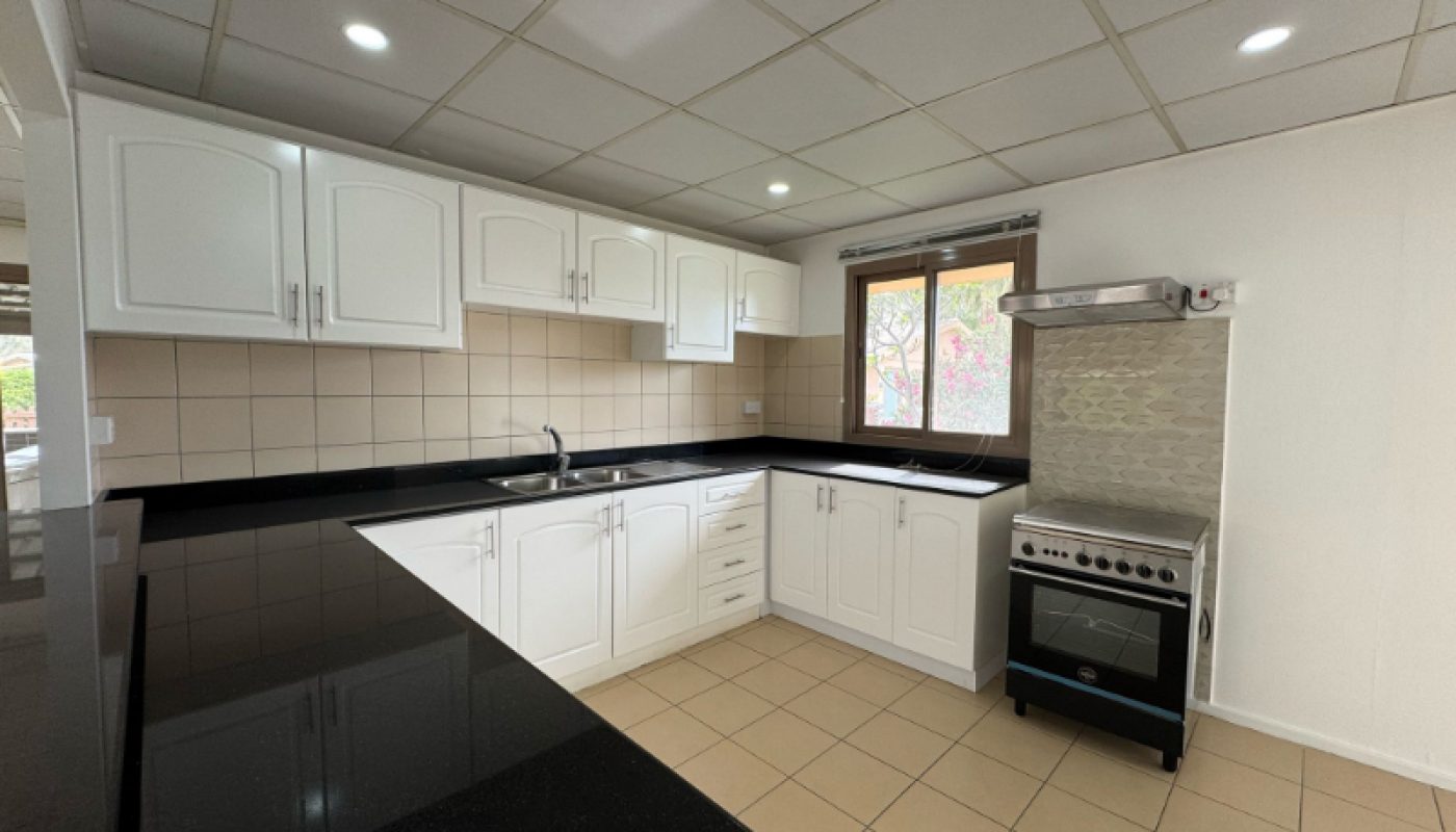 Modern kitchen with white cabinets, black countertops, tan tile floor, stainless steel stove, and a window above the sink.