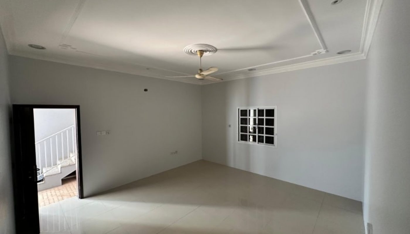 An empty room with white walls, a ceiling fan, tiled floor, a window, and an open door leading to a stairway outside.