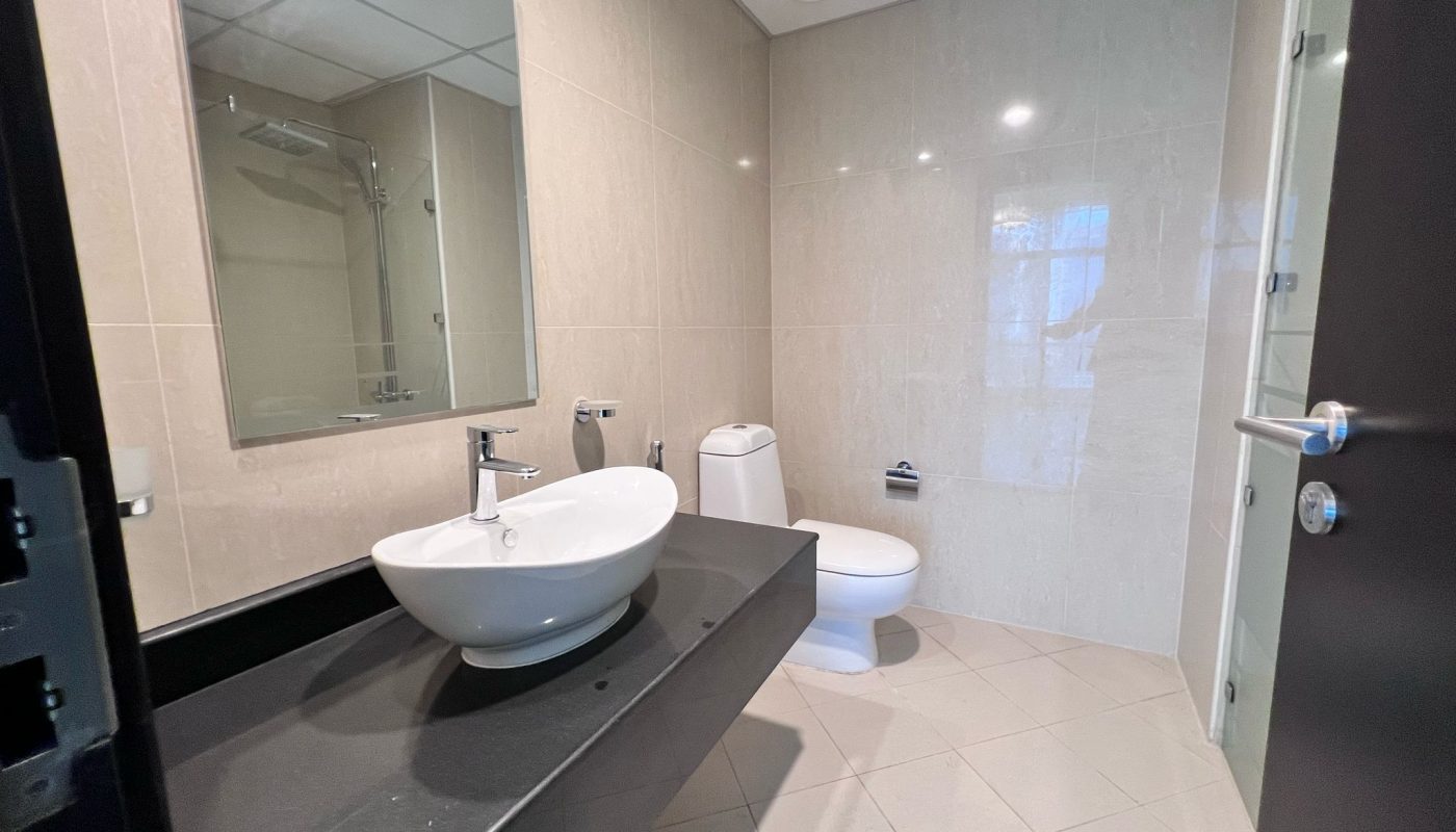 Modern bathroom with beige tiles, a white vessel sink on a black countertop, a wall mirror, toilet, and glass shower door.