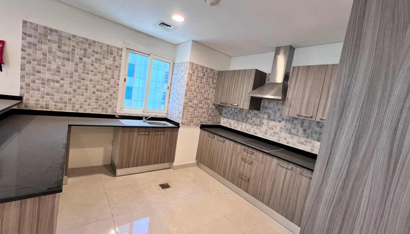 Modern kitchen with wood-patterned cabinets, black countertops, tiled backsplash, built-in stove with range hood, and a window providing natural light.