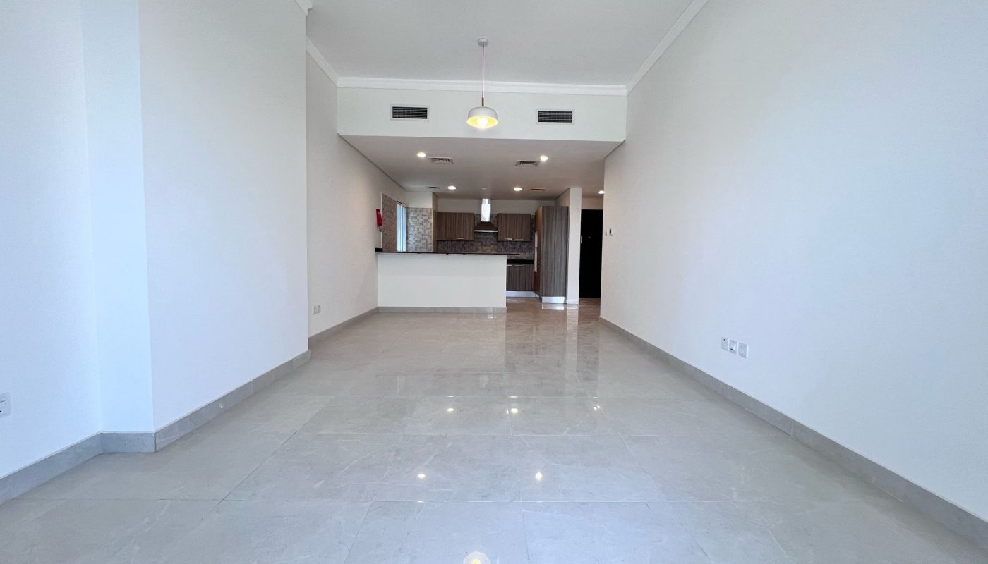 Unfurnished apartment with white walls, tiled floors, two ceiling lights, open-plan kitchen, and visible built-in cabinets in the background.