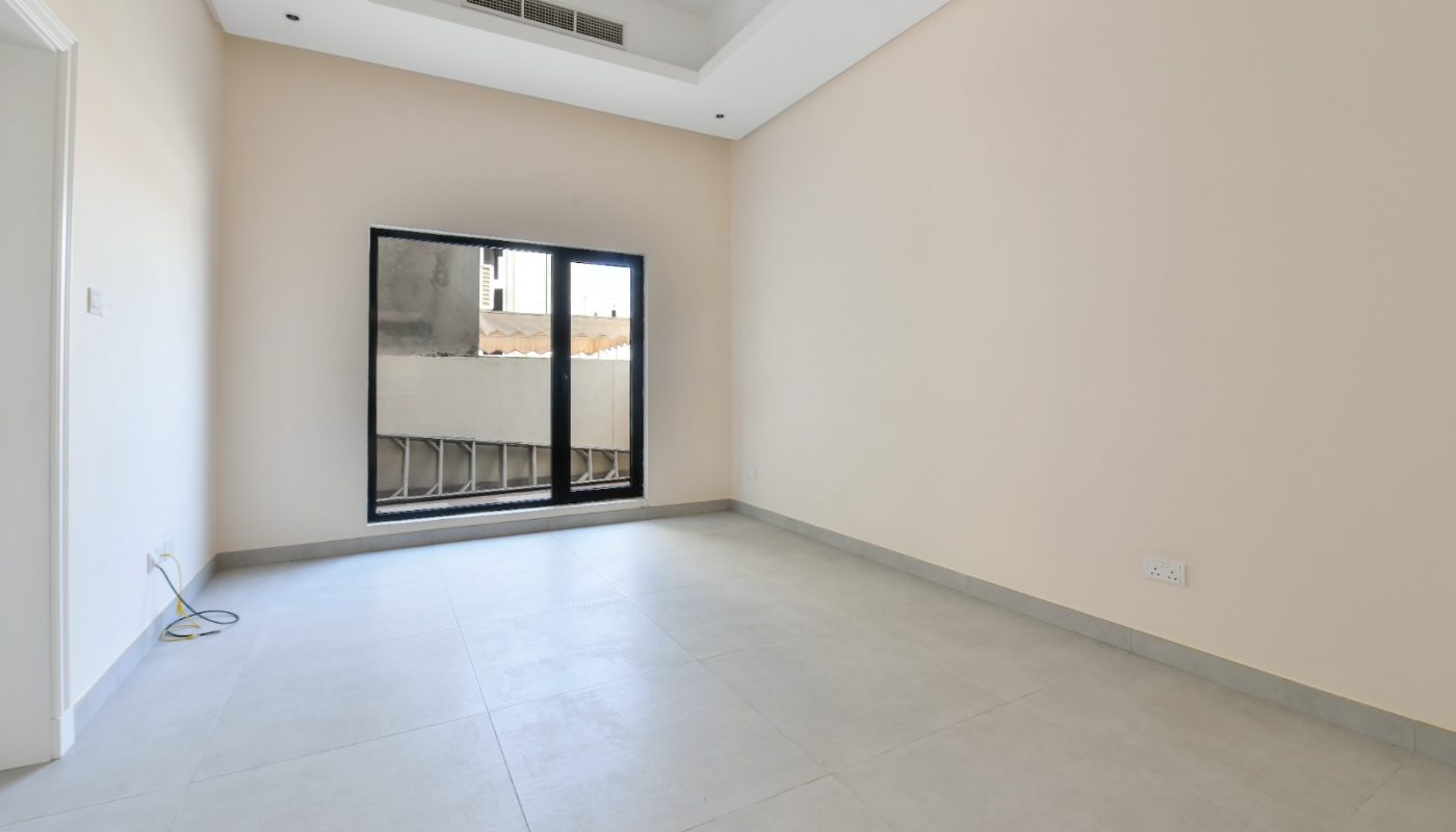 Empty room with beige walls, large window, tiled floor, and a white ceiling with recessed lighting and an air vent. Electrical outlets and a cable are visible near the window.