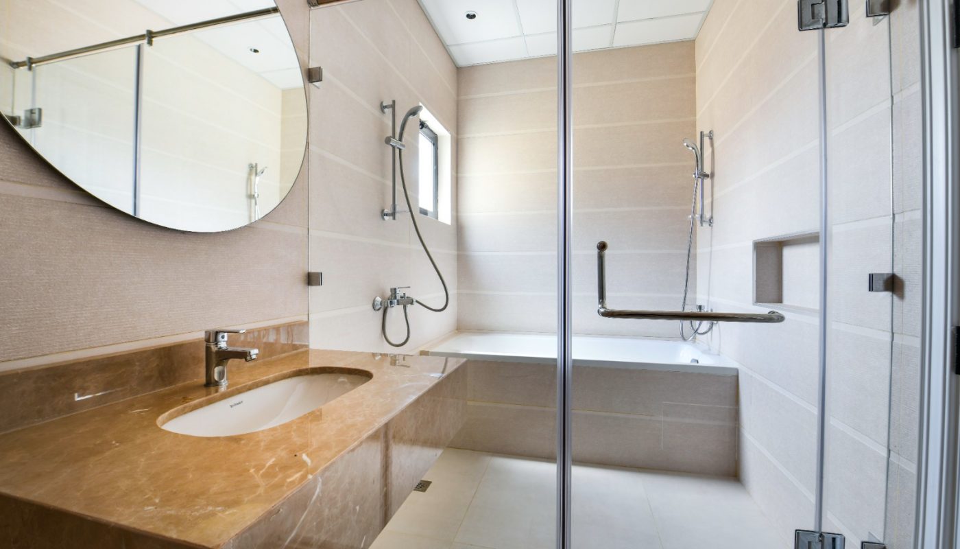 Modern bathroom with beige tiles, a glass-enclosed shower, bathtub, large mirror, and a brown marble countertop with a sink.