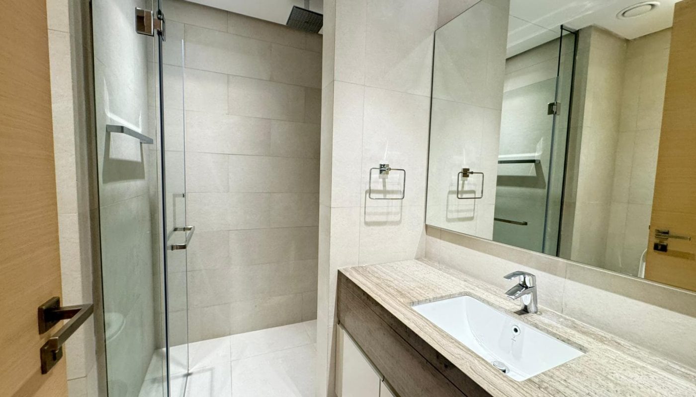 Modern bathroom with a glass-enclosed shower, large mirror, beige tiles, and a sink with a wooden vanity and metal faucet.