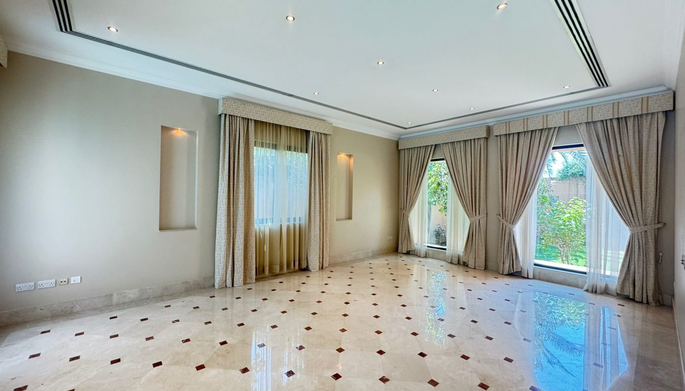 Spacious empty room with marble tile floor, large windows draped with beige curtains, and natural light streaming in from the garden outside.
