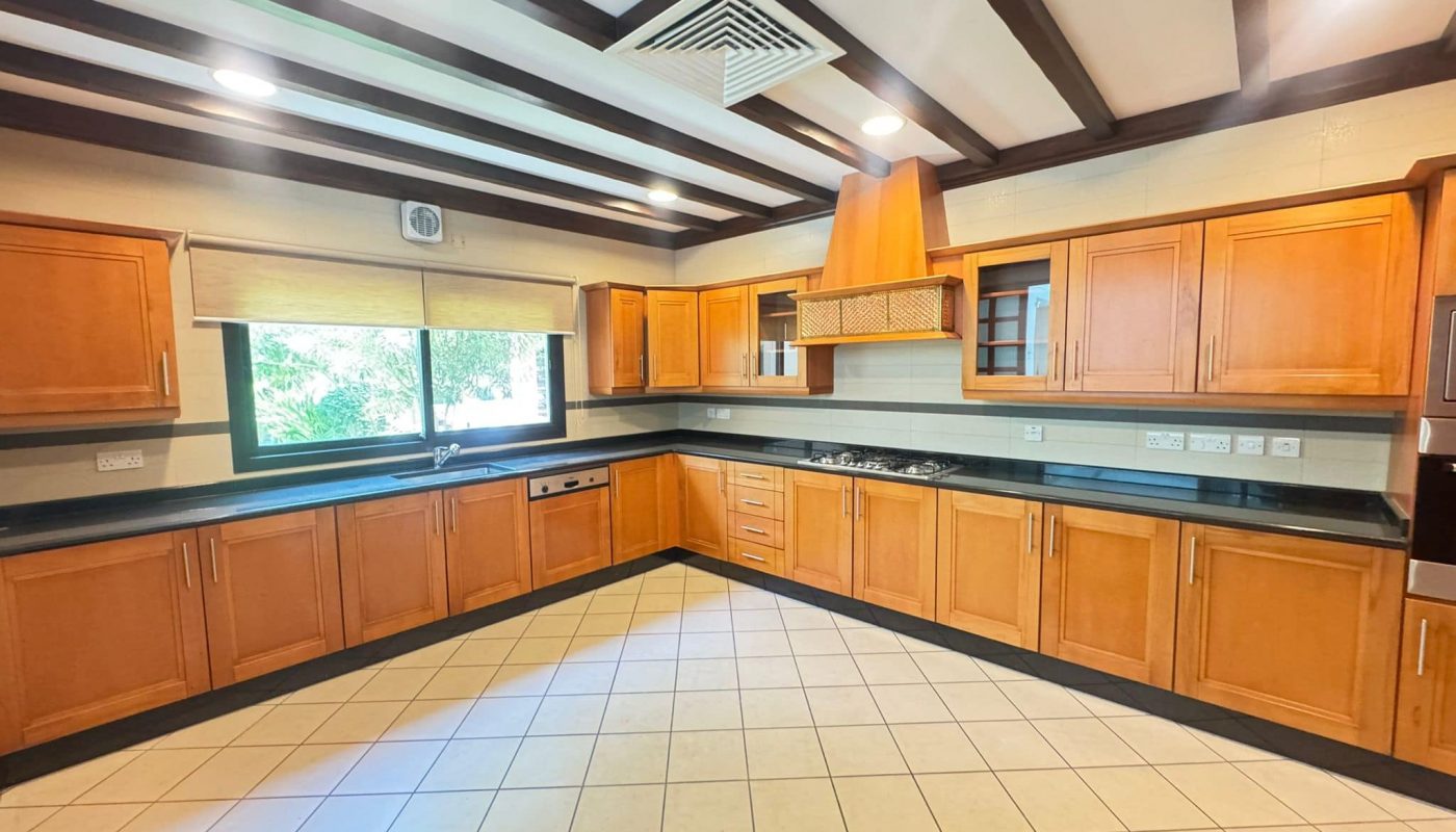 Spacious kitchen with wooden cabinets, black countertops, tiled floor, large window, built-in stove, and overhead vent.