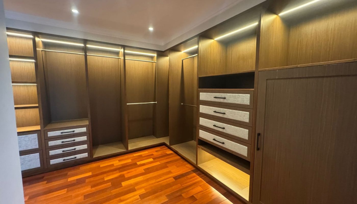 Spacious walk-in closet with built-in wooden shelves, drawers, and cabinets, illuminated by recessed lighting, and a polished wooden floor.