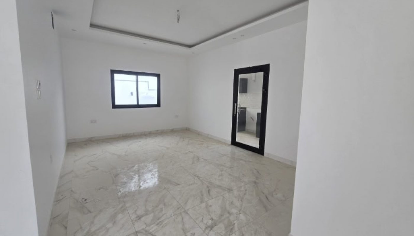 Empty, unfurnished room with white walls, marble tile floor, a window on one side, and a black-framed glass door leading to an adjacent room.