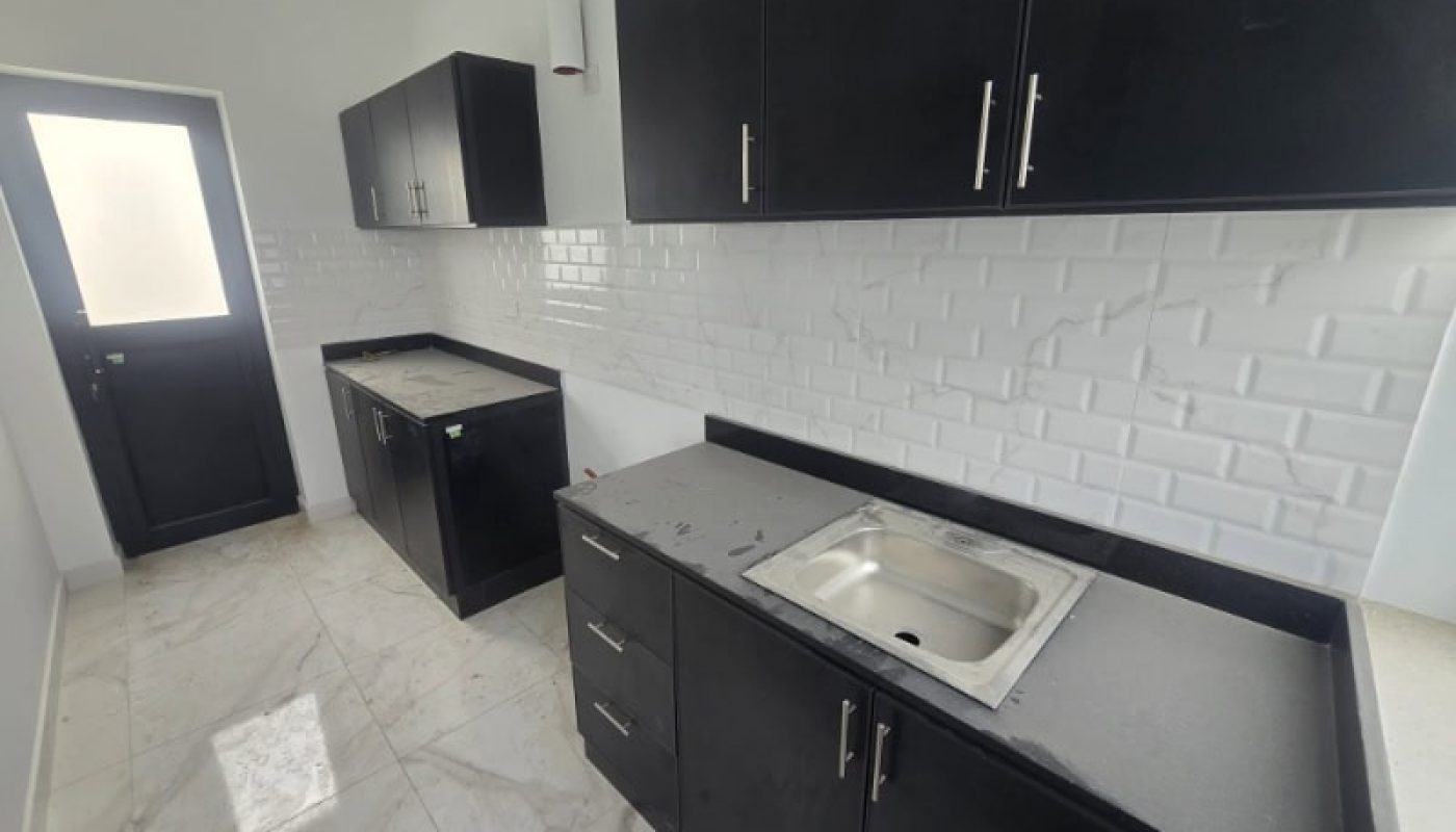 A modern kitchen with black cabinets, white tiled backsplash, marble floor, a stainless steel sink, and a frosted glass door.