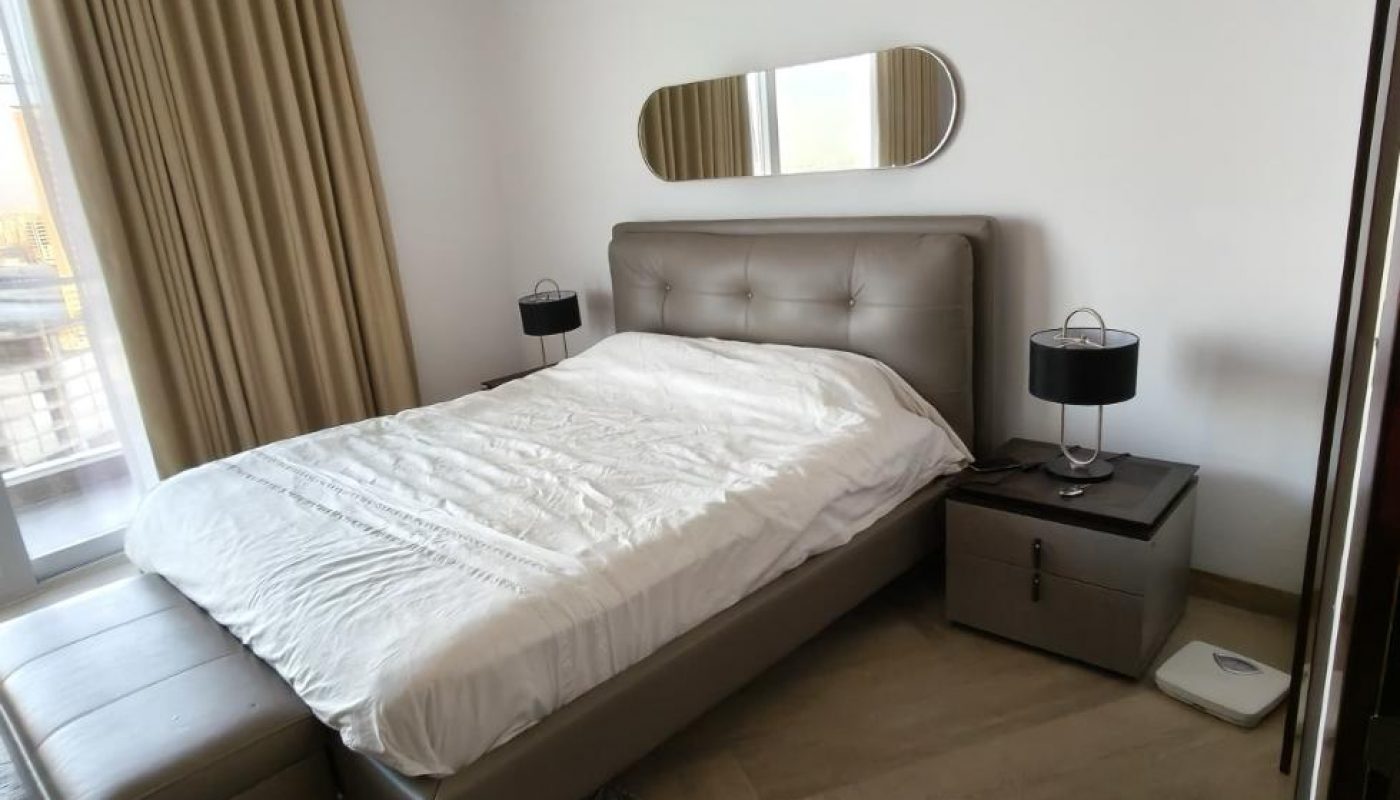 A modern bedroom with a double bed, two bedside tables with lamps, beige curtains, a rug, and a wall mirror above the headboard.