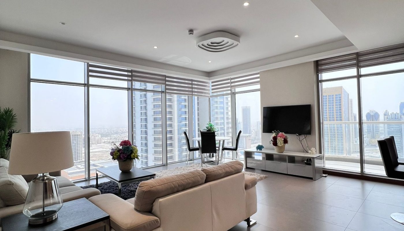 Modern living room with large windows, light-colored sofa, dining table, TV, and city skyline views in the background.