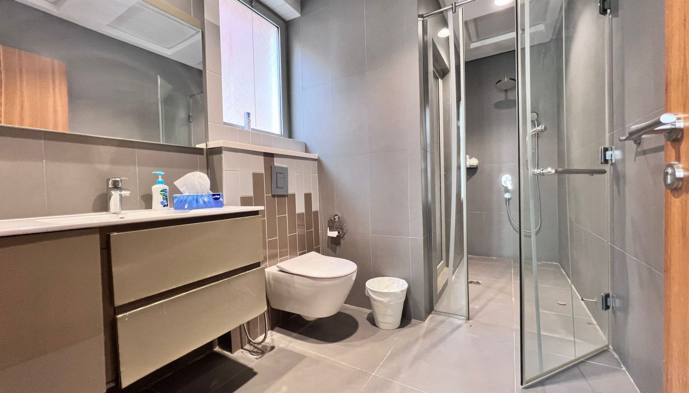 Modern bathroom with a wall-mounted sink and toilet, a glass-enclosed shower, a mirror, and neutral gray tiles throughout.