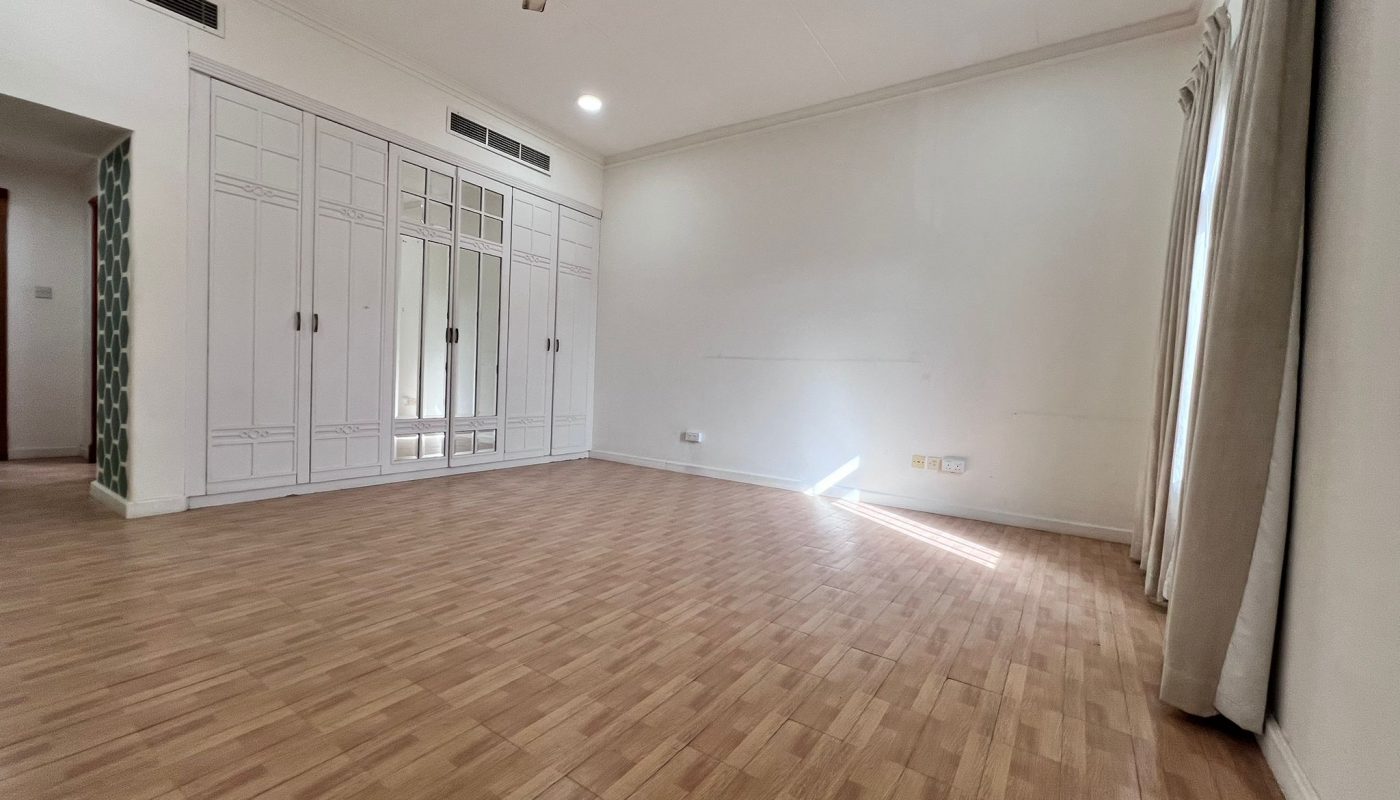 Spacious empty room with wooden flooring, white built-in wardrobes with mirrors, ceiling fan, and a window with curtains letting in natural light.