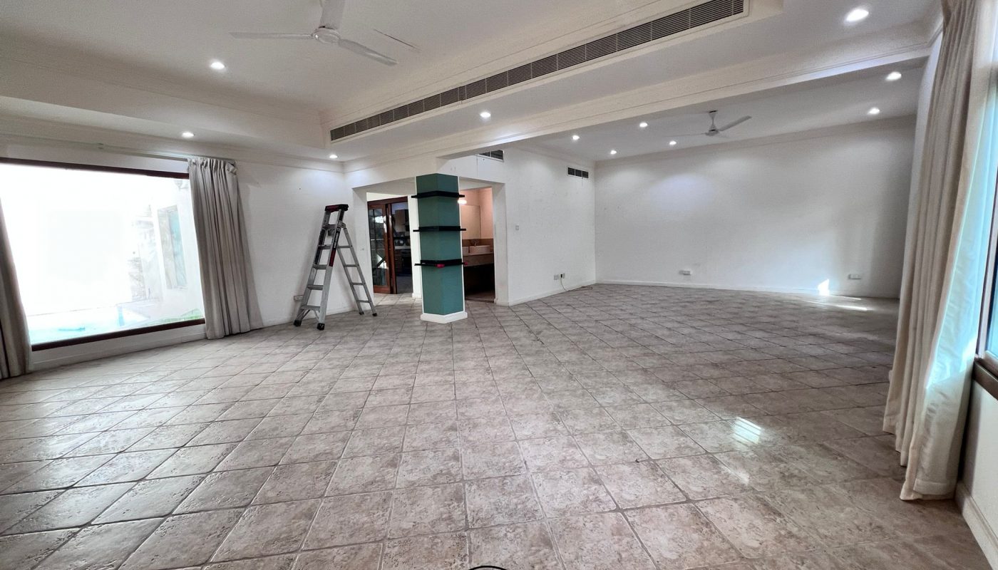 Spacious, empty room with tiled floor, ceiling fans, recessed lighting, a step ladder, large windows, and an open doorway to a kitchen area.