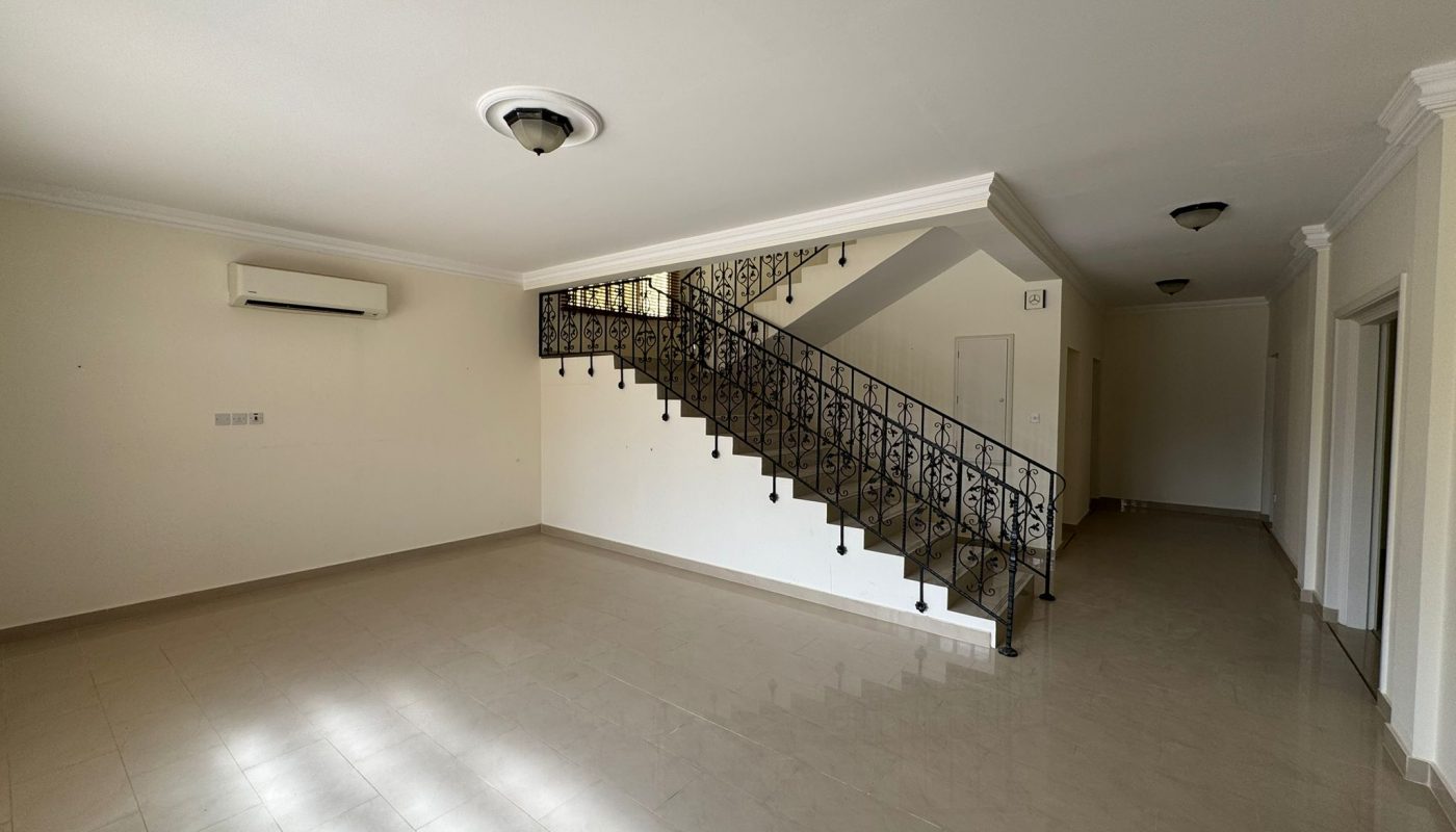Empty, unfurnished room with tiled flooring, a black metal staircase, air conditioning unit on the wall, and multiple doors along a hallway.