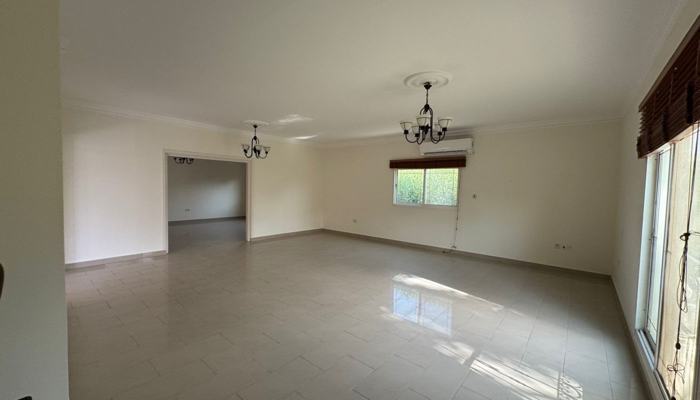 Spacious, empty living room with tiled floor, two windows, ceiling lights, and an air conditioning unit mounted on the wall.