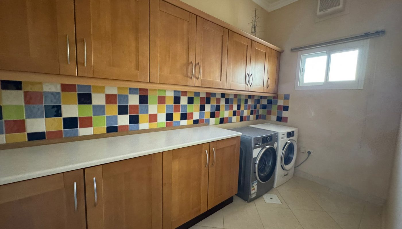 Laundry room with wooden cabinets, a colorful tiled backsplash, a washing machine, a dryer, and a small window on the right wall.
