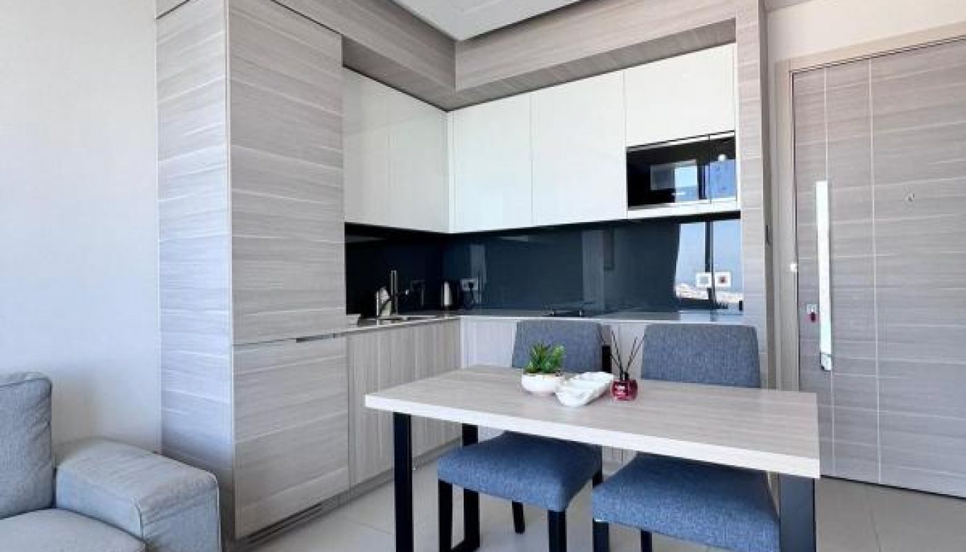 Modern compact kitchen and dining area with a small table, two chairs, light wood cabinets, and minimalistic decor in a bright apartment.