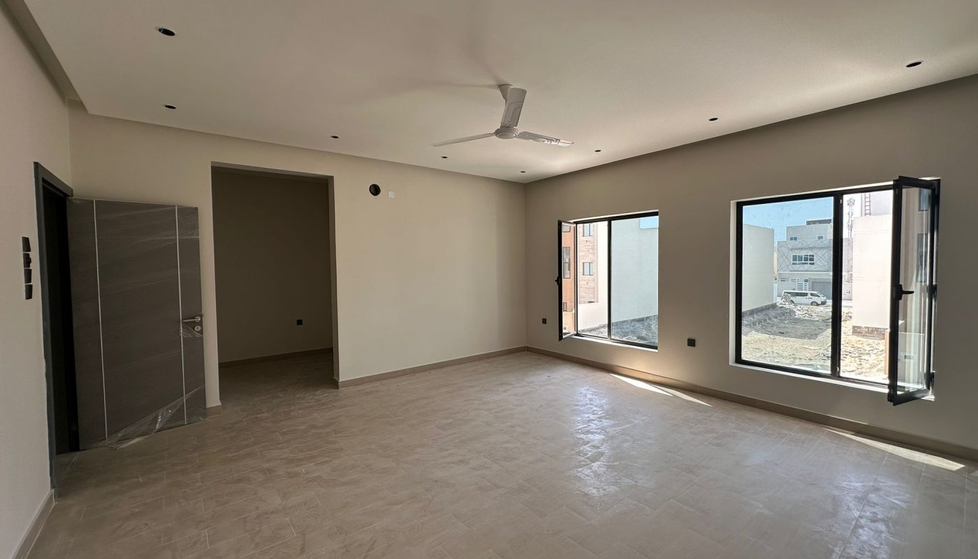 Empty, unfurnished room with tiled floor, white walls, ceiling fan, recessed lights, open door, and two large windows letting in natural light.