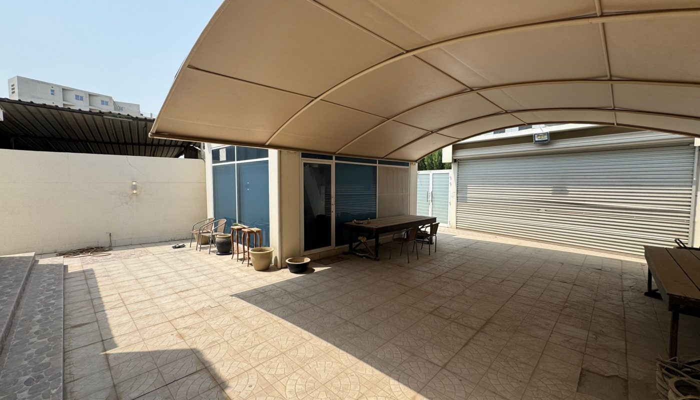Spacious covered patio with tiled floor, a table with chairs, and a closed garage door; building and outdoor items visible.