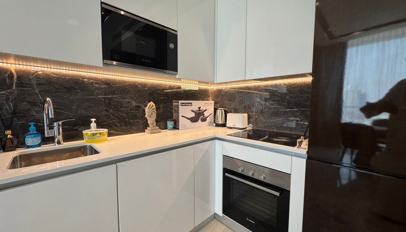 Modern kitchen with white cabinets, black marble backsplash, built-in appliances, a sink, and various items on the countertop including soap, sponge, and a kitchen gadget box.