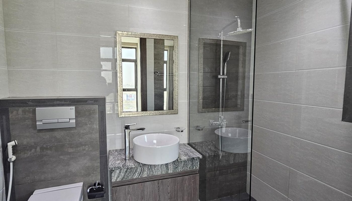 Modern bathroom with a wall-mounted toilet, vessel sink on a marble countertop, glass shower enclosure, and a large mirror above the sink.