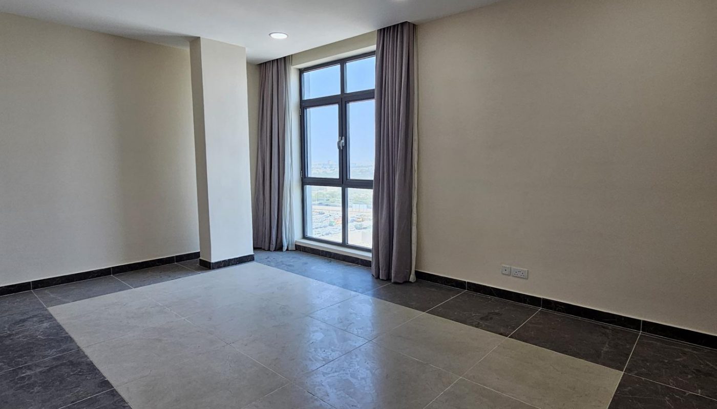 Empty room with beige walls, a large window with closed curtains, and a floor with a central light-colored tile section bordered by dark tiles.