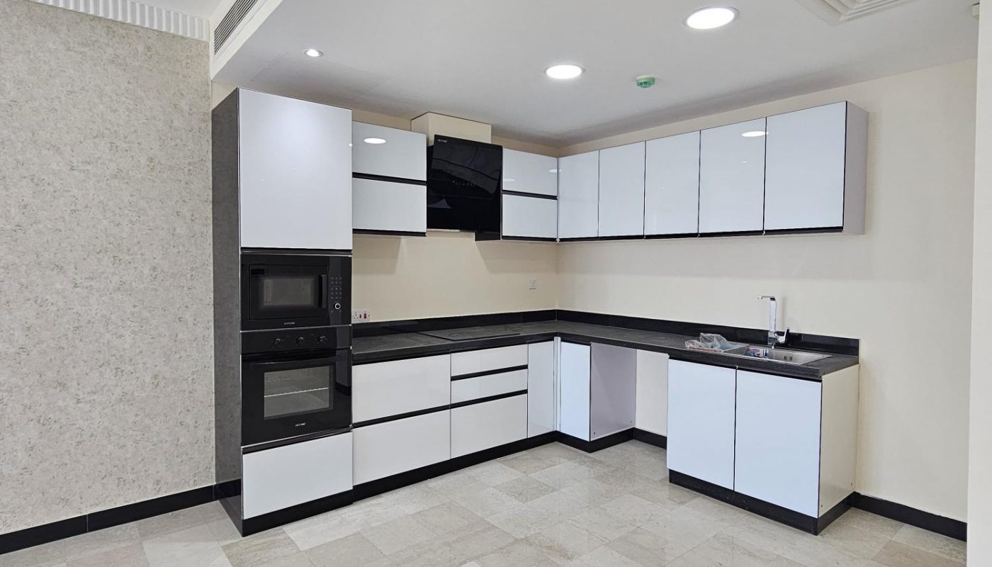 Modern L-shaped kitchen with white cabinets, black countertops, built-in appliances, tiled floor, and recessed lighting in a spacious room.