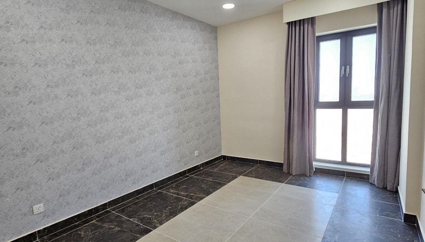 Empty room with tiled floor, accent wall, recessed lighting, and a window covered by sheer curtains letting in natural light.