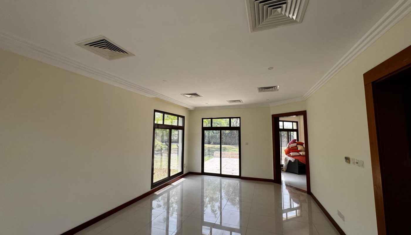 Empty, unfurnished room with white tile floor, cream-colored walls, and large windows providing natural light; a doorway opens to a garage with a red car visible.