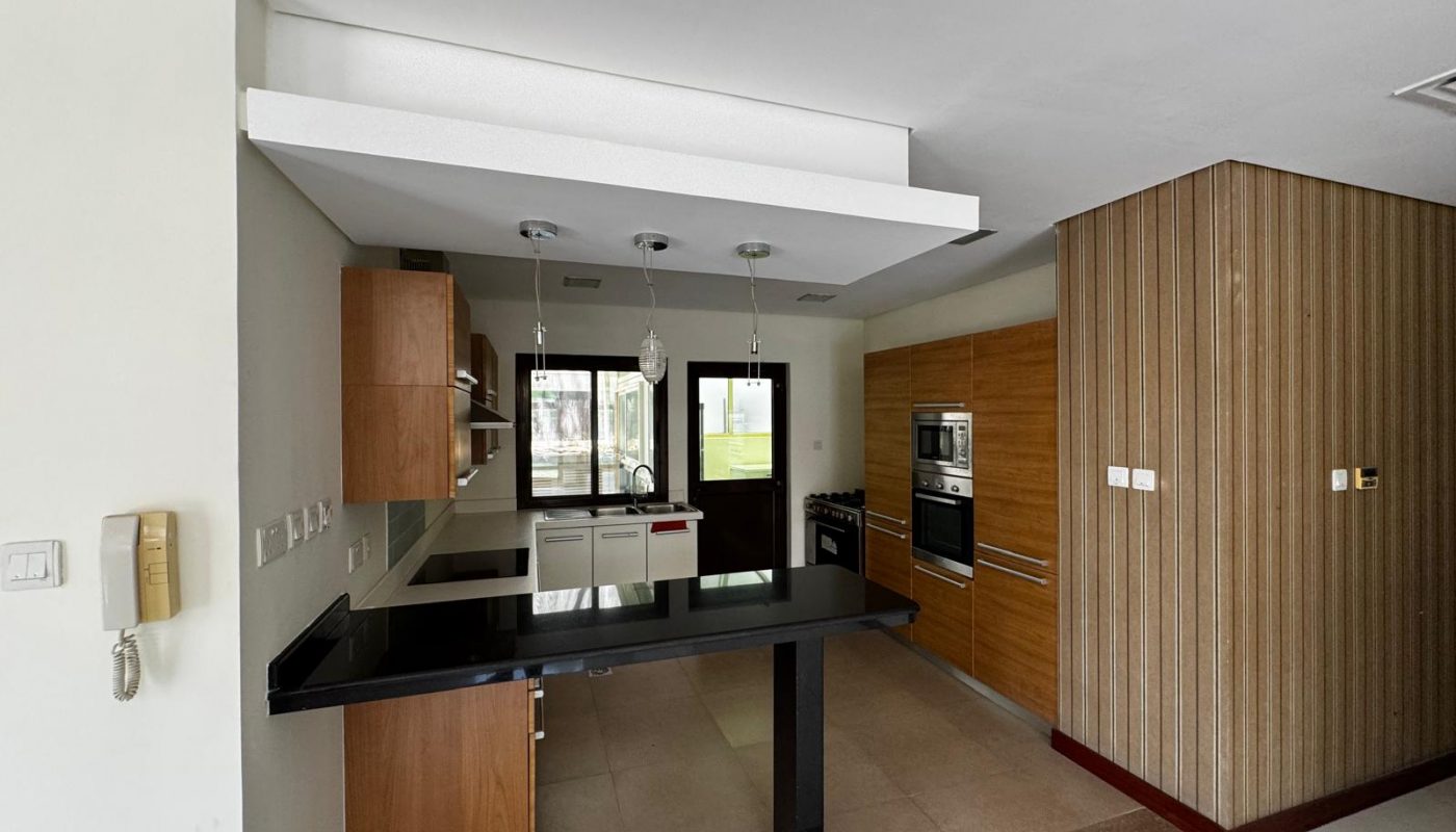 Modern kitchen with wooden cabinets, built-in appliances, black countertop island, pendant lights, and large windows providing natural light.
