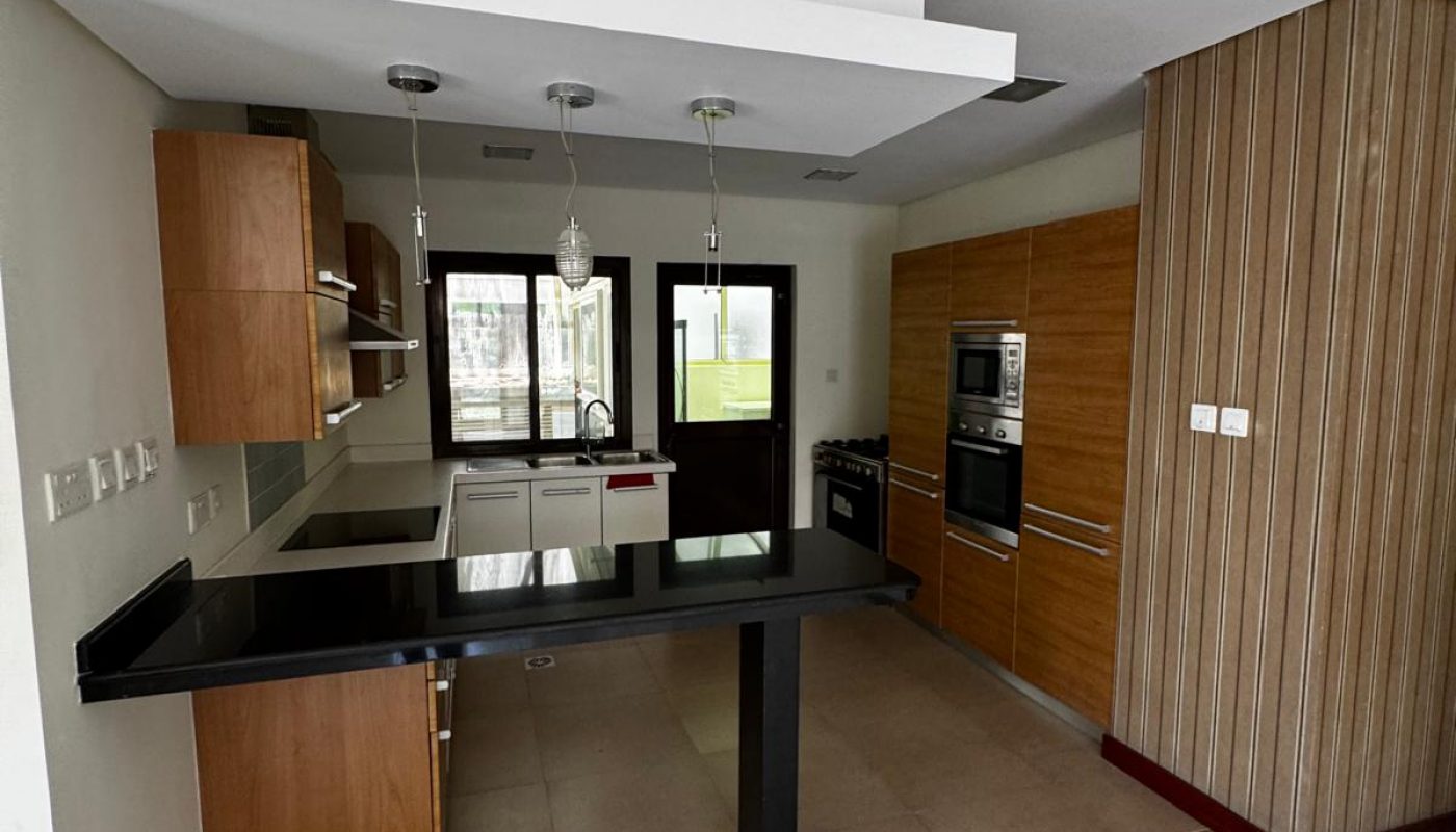 Modern kitchen with wooden cabinets, black countertop, built-in oven, stove, hanging lights, and a large windowed door at the back.