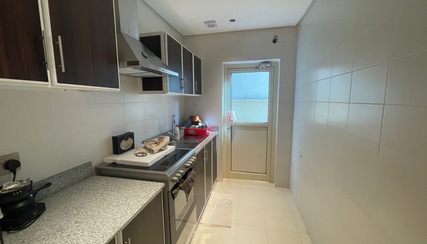 Narrow kitchen with dark cabinets, stainless steel appliances, a countertop with utensils, and a door leading to a frosted glass window.