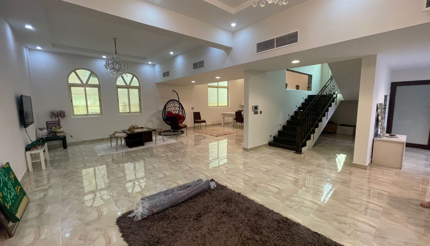 Spacious living room with marble floors, modern furniture, a large staircase, chandeliers, and multiple windows letting in natural light.