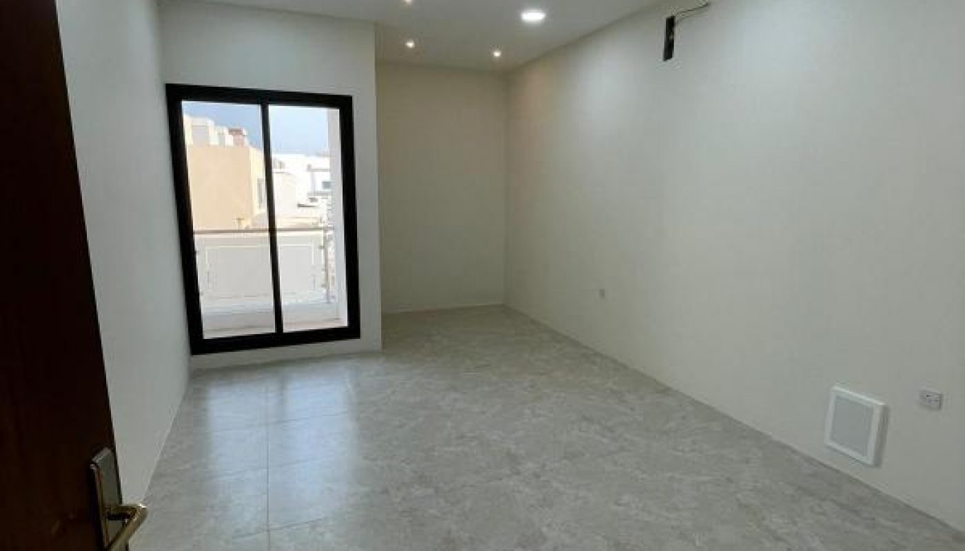 Empty, unfurnished room with tiled floor, white walls, recessed ceiling lights, a sliding glass door leading to a balcony, and a wall-mounted air conditioning unit.
