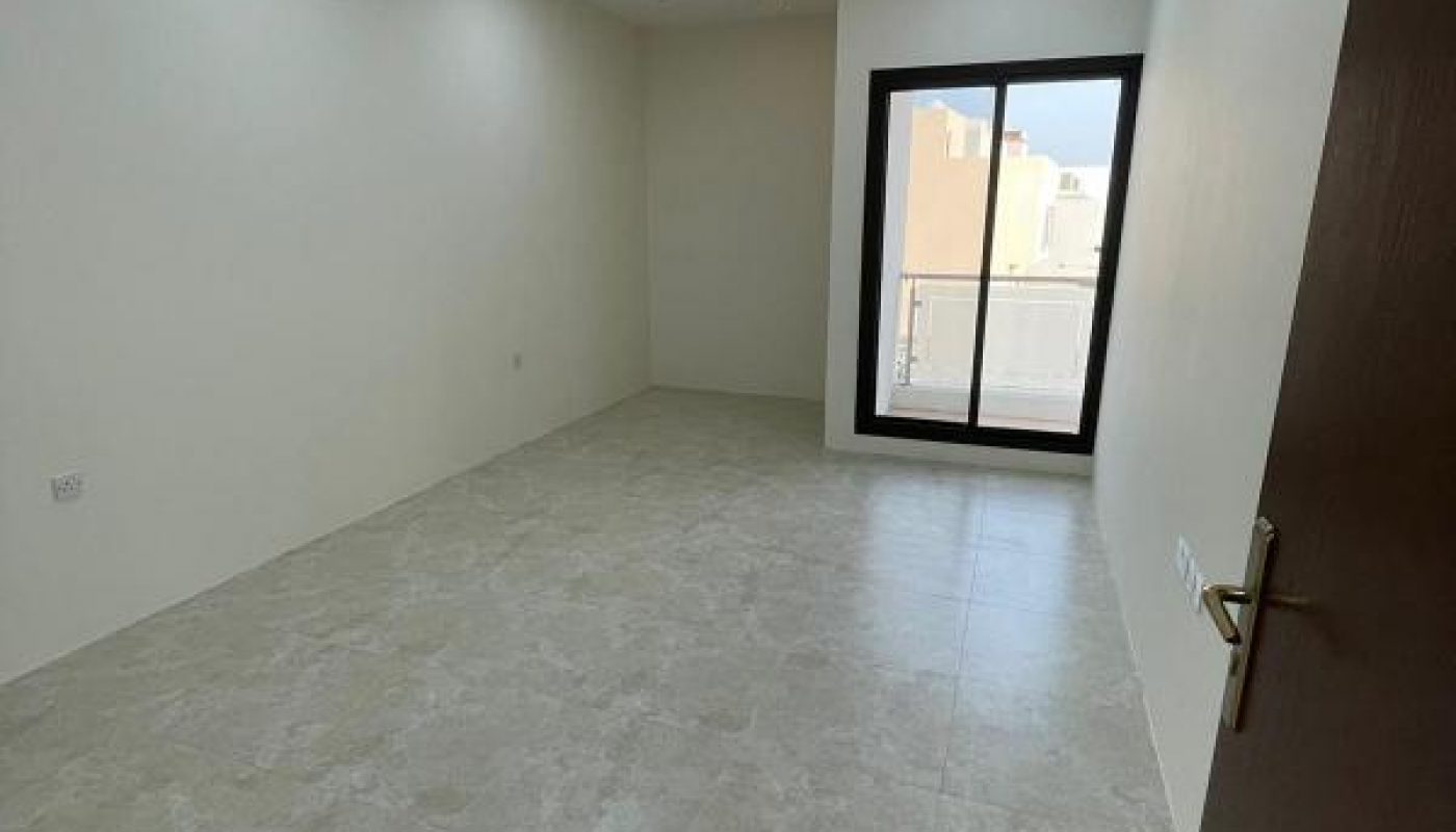 Empty, unfurnished room with tiled floor, white walls, recessed ceiling lights, and a glass door leading to a small balcony with an outdoor view.