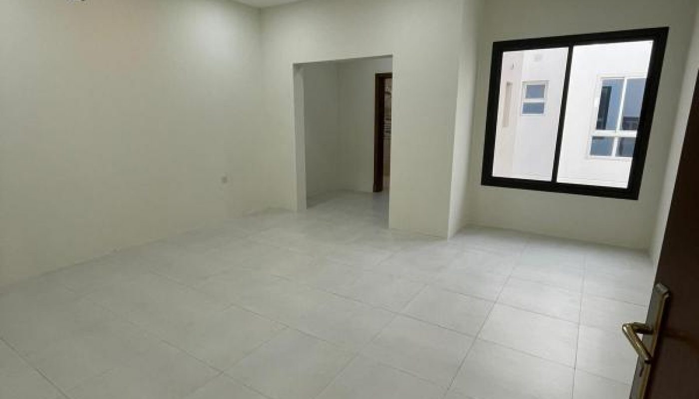 Empty room with white tiled floor, white walls, recessed ceiling lights, a large window, and an open doorway leading to another area.