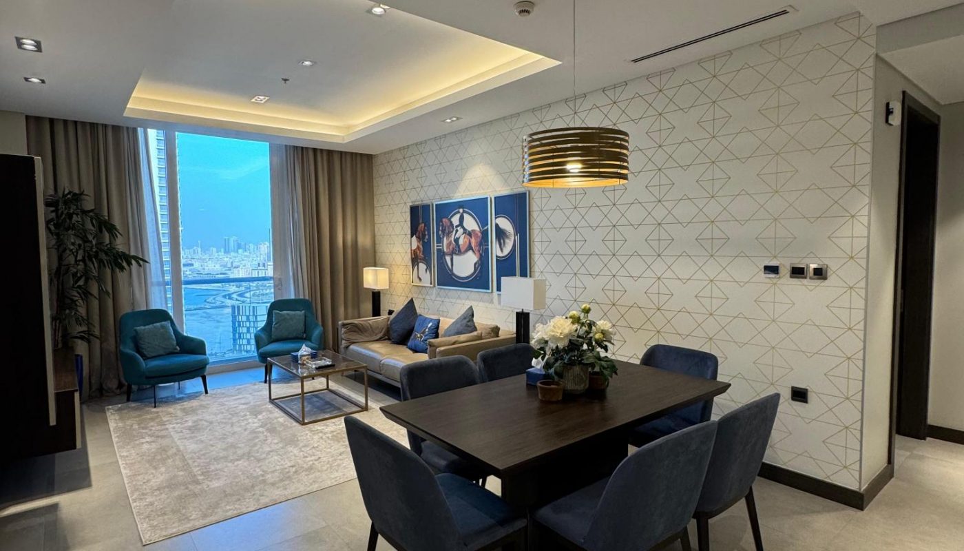 Modern open-plan living and dining area with blue chairs, a dark dining table, wall art, large windows, and city views.