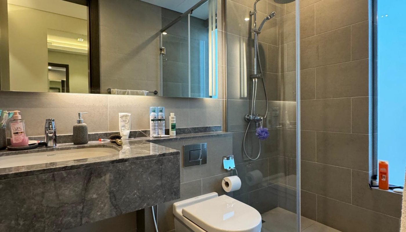 Modern bathroom with gray tiles, a large mirror, floating sink, wall-mounted toilet, and glass-enclosed shower area with overhead and handheld showerheads.