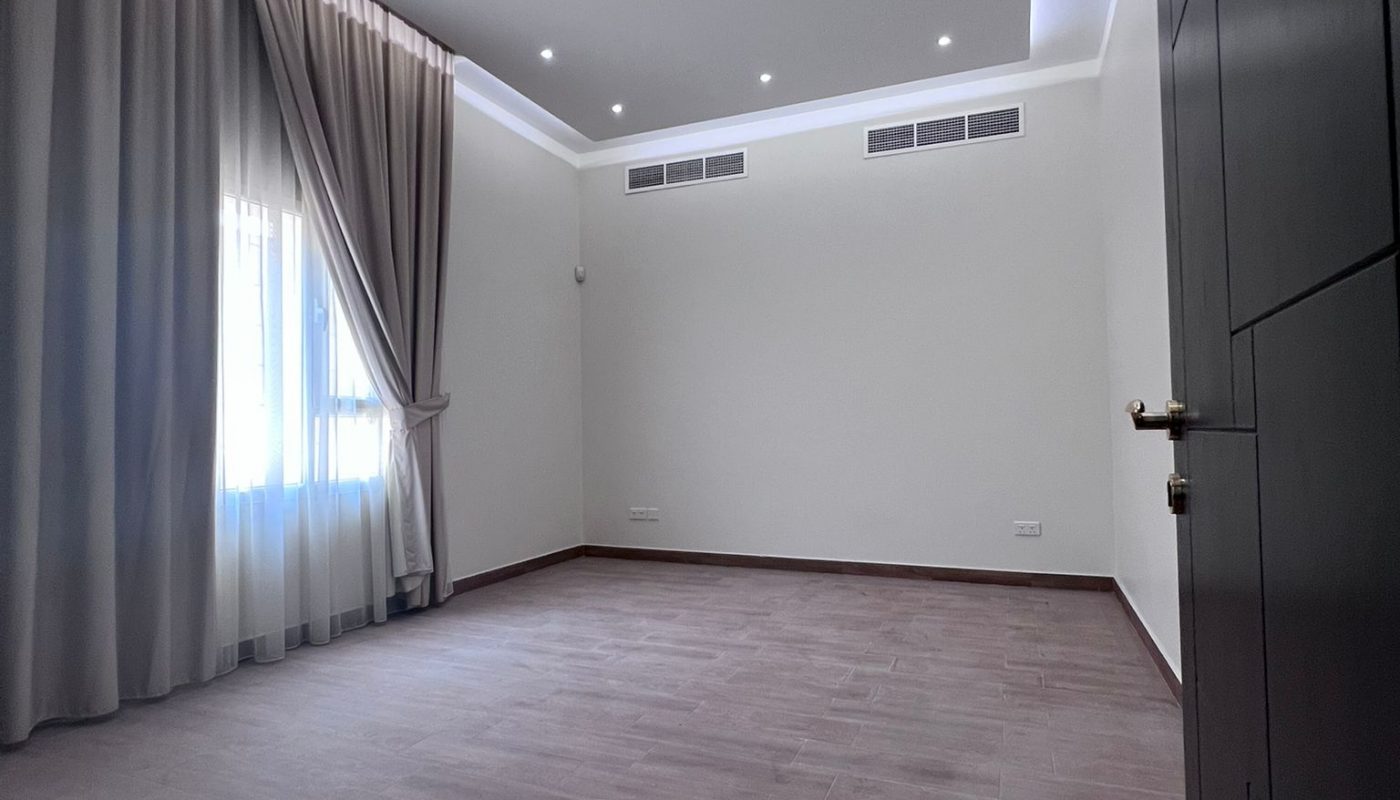 Empty room with wood flooring, beige walls, a window covered by sheer and opaque curtains, recessed ceiling lights, and air vents along the far wall.