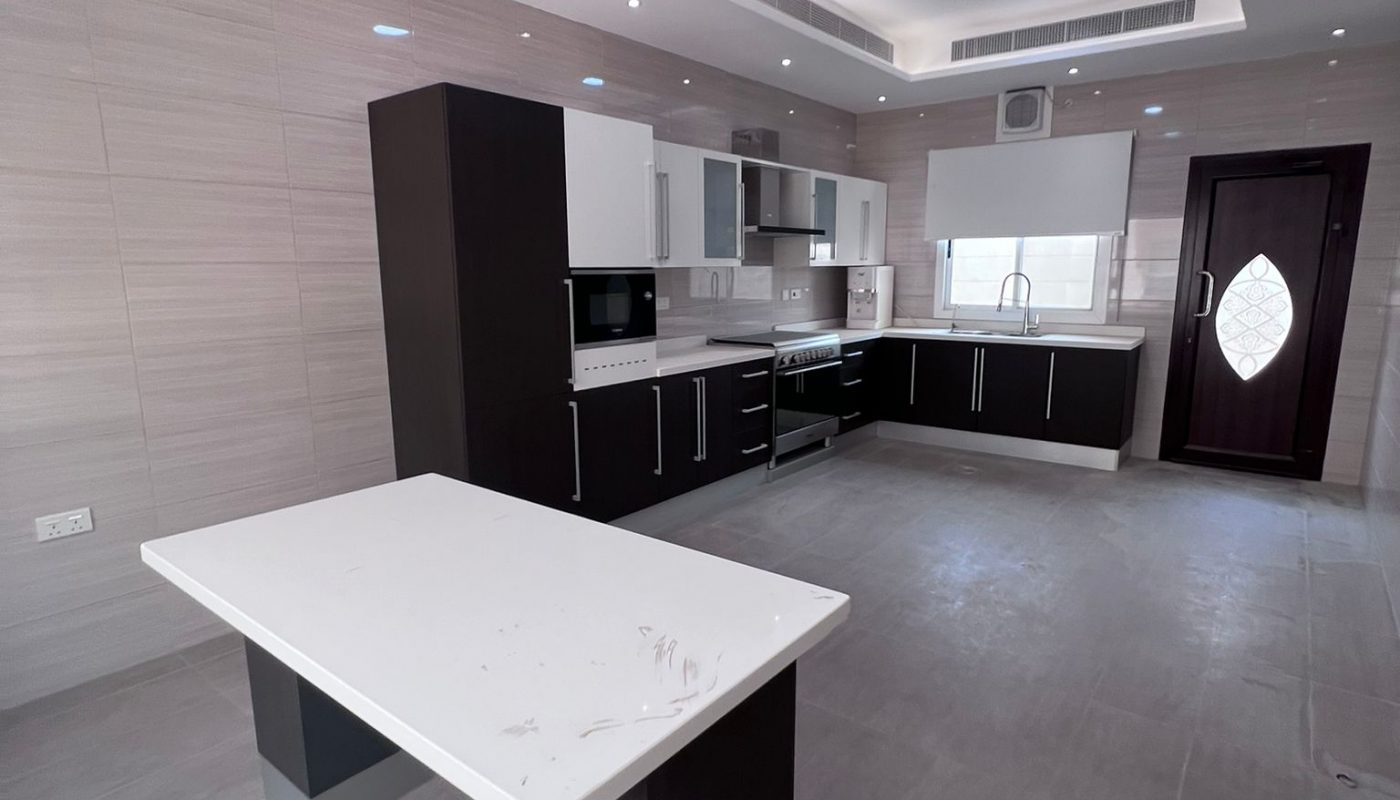 Modern kitchen with dark cabinets, light countertops, built-in appliances, a central island, tiled walls and floor, and a door with a geometric window.